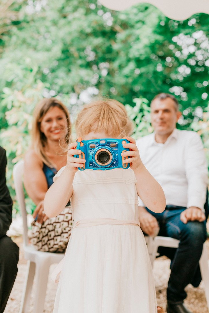 Une petite fille photographie ses parents avec un appareil, lors d'un mariage